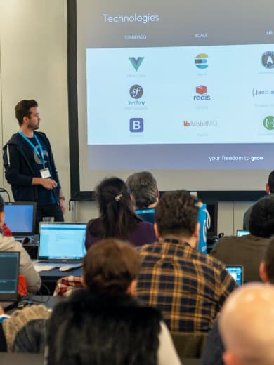 Shopware Mitarbeiter hält eine Präsentation über Technologien wie Vue.js oder Symfony zu Shopware Hackathon Teilnehmern.
