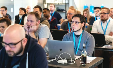Eine Gruppe von Hackathon-Teilnehmern hört aufmerksam einer Präsentation zu.

