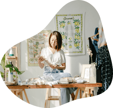 Eine Frau sitzt an einem Holztisch und begutachtet verschiedene Stoffe.